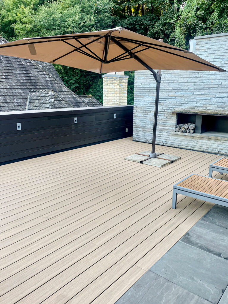 Spacious outdoor patio with lounge chairs, a large umbrella, and surrounded by trees under a clear sky.