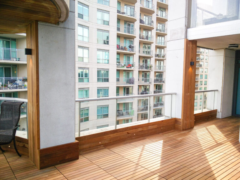 Modern apartment balcony with IPE wooden flooring, glass railing, and views of neighboring balconies.