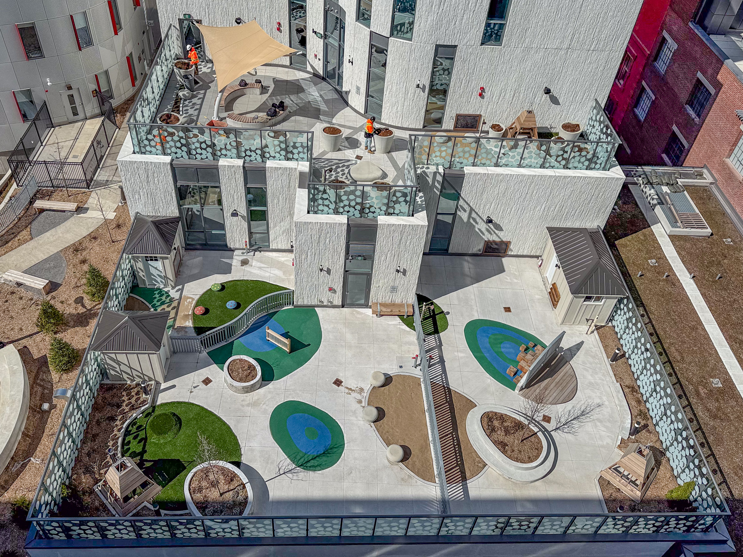 Aerial view of a modern outdoor playground with artificial turf, benches, and play structures on a rooftop terrace.