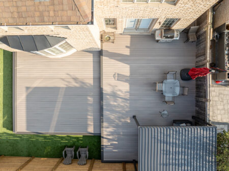 Aerial view of a backyard deck with patio furniture, umbrella, and shaded area next to a brick house.