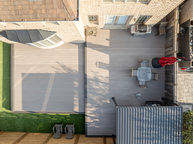 Aerial view of a backyard deck with patio furniture, umbrella, and shaded area next to a brick house.