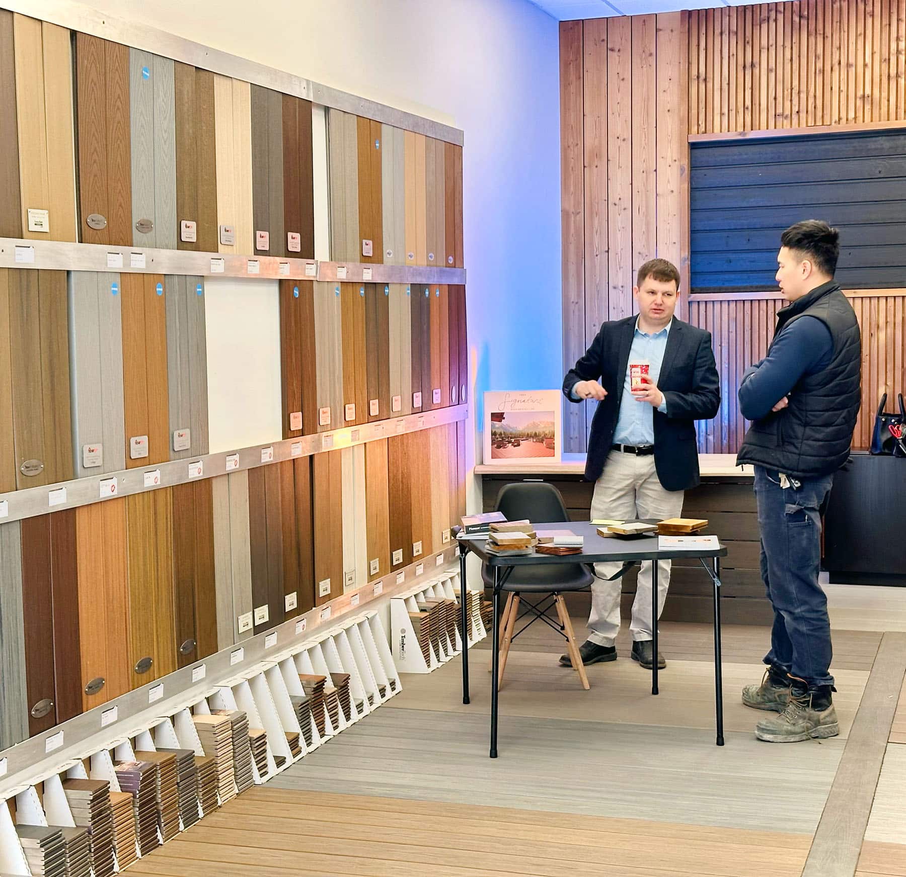 Two men discuss various composite deck samples adorning the walls in the Composite Deck Store showroom steeped in craftsmanship.